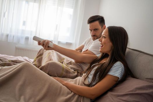 Young couple is watching tv in their bedroom.