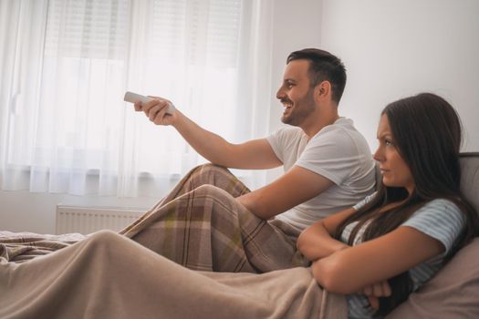 Young couple is watching tv in their bedroom.