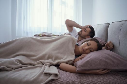 Young couple is sleeping in bed. Man is waking up for work.