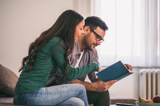 Happy couple is sitting at sofa in their home and relaxing.