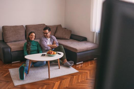 Young couple is watching tv at home. Man is not satisfied with tv program.