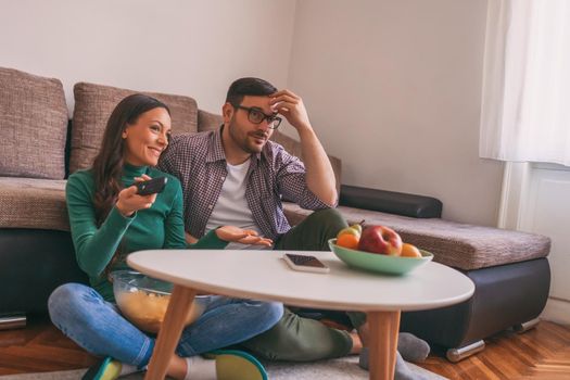 Young couple is watching tv at home. Man is not satisfied with tv program.