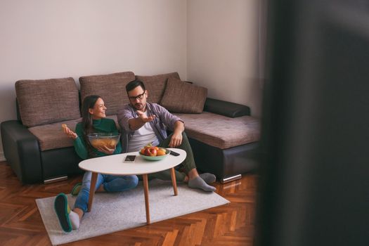 Young couple is watching tv at home. Man is not satisfied with tv program.