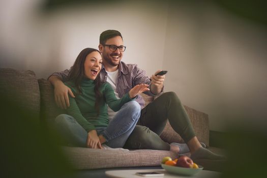 Happy couple in love is relaxing at home. They are watching tv.