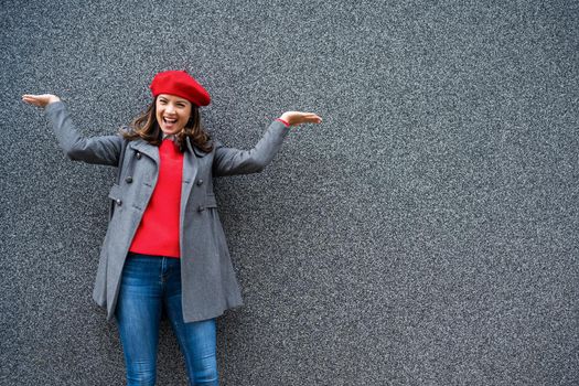 Adult woman in modern casual clothing standing in front of gray background. She is cheerful and looking at camera. Copy space for your advert.