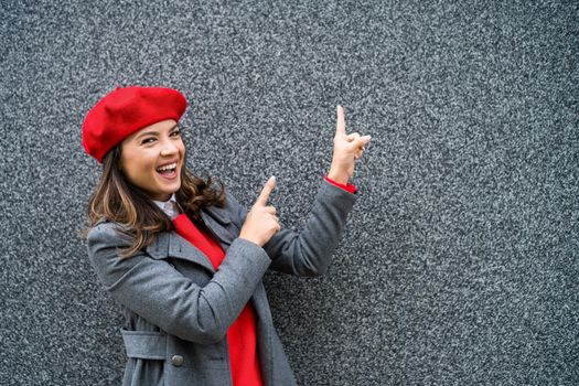 Adult woman in modern casual clothing standing in front of gray background. She is pointing at copy space for your advert.