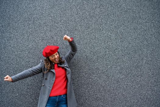 Adult woman in modern casual clothing standing in front of gray background. She is ecstatic. Copy space for your advert.