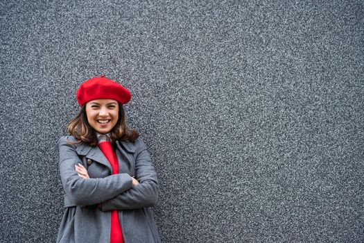 Adult woman in modern casual clothing standing in front of gray background. She is cheerful and looking at camera. Copy space for your advert.