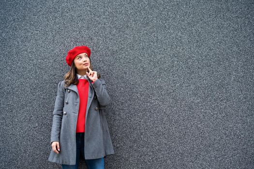 Adult woman in modern casual clothing standing in front of gray background. She is pensive and looking away. Copy space for your advert.