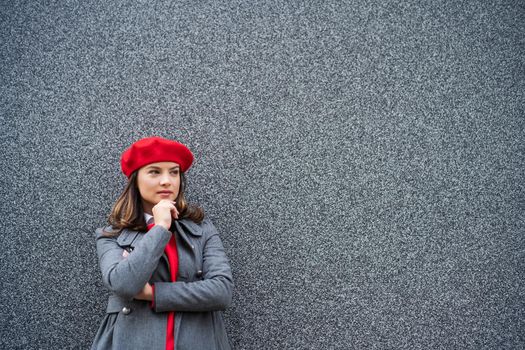 Adult woman in modern casual clothing standing in front of gray background. She is pensive and looking away. Copy space for your advert.