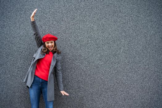 Adult woman in modern casual clothing standing in front of gray background. She is ecstatic. Copy space for your advert.