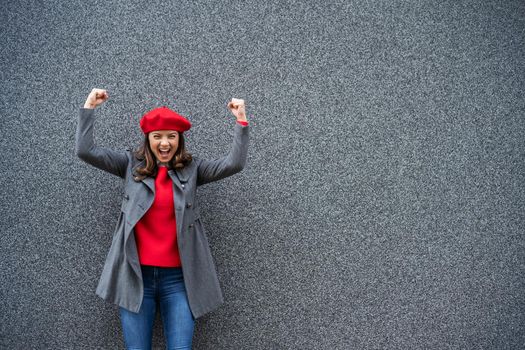 Adult woman in modern casual clothing standing in front of gray background. She is ecstatic. Copy space for your advert.