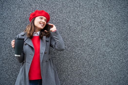 Adult woman in modern casual clothing standing in front of gray background. She is talking on phone. Copy space for your advert.