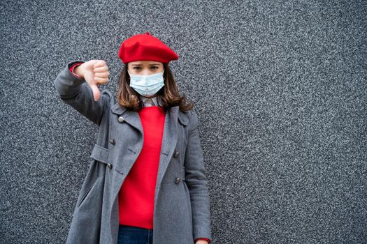 Adult woman in modern casual clothing standing in front of gray background. She is wearing protective mask. Copy space for your advert.