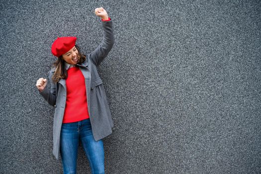 Adult woman in modern casual clothing standing in front of gray background. She is ecstatic. Copy space for your advert.