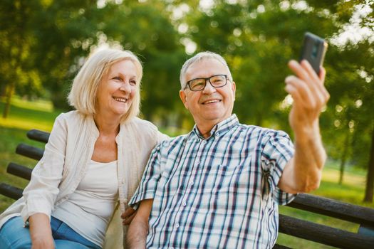 Happy senior couple is using smartphone in park. They are taking selfie.