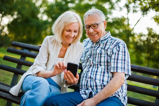 Happy senior couple is using smartphone in park.