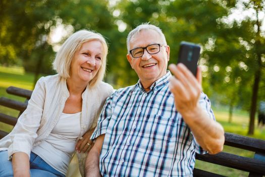 Happy senior couple is using smartphone in park. They are taking selfie.