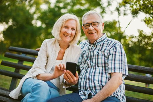 Happy senior couple is using smartphone in park.