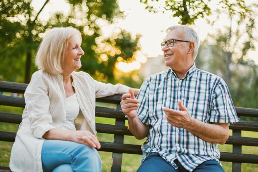 Two happy seniors are sitting and talking in park.