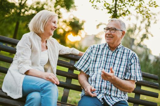 Two happy seniors are sitting and talking in park.