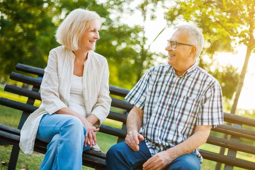 Two happy seniors are sitting and talking in park.