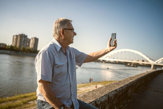 Outdoor portrait of senior man who is taking selfie.