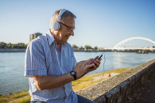 Outdoor portrait of senior man who is listening music on headphones.