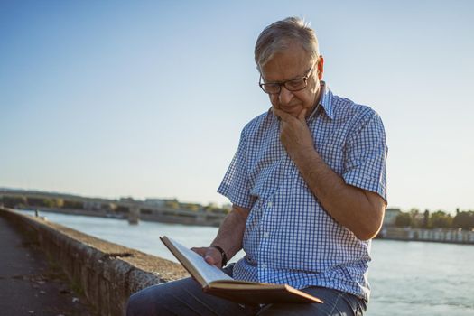 Outdoor portrait of senior man who is reading a book.