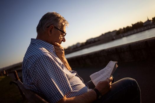 Outdoor portrait of senior man who is reading newspapers.