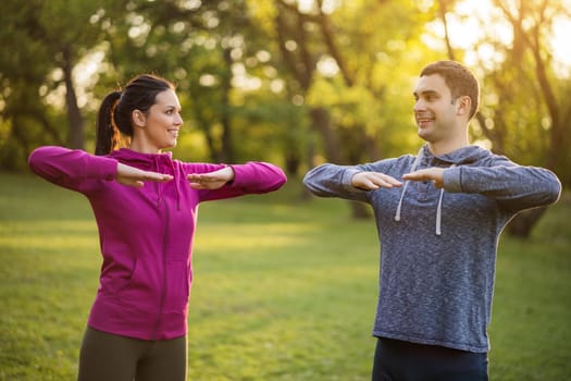 Happy couple is exercising in park. They are stretching their bodies.