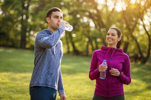 Young couple exercising in park. They are drinking water.