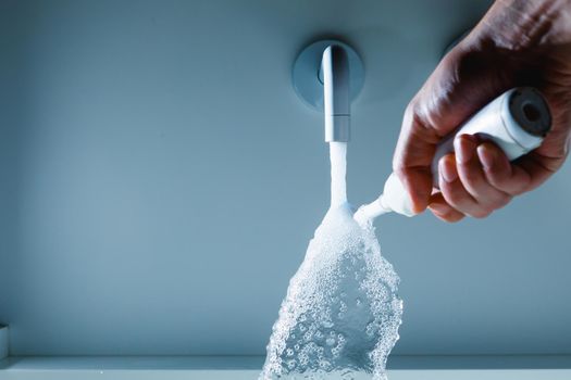 hand holding toothbrush under flowing water from faucet in a bathroom