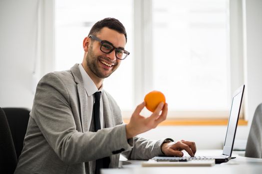 Young businessman is eating orange as snack.