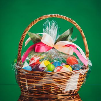 Easter gift basket with multicolor eggs, green background