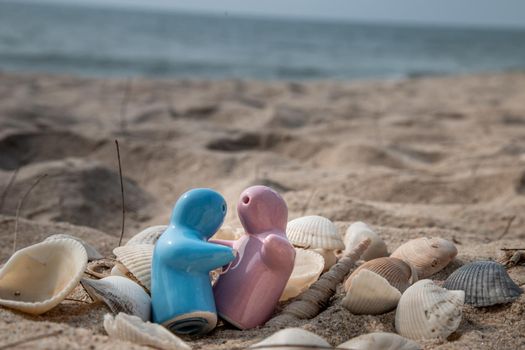 Ceramic couple dolls and shells in sand on the beach and copy space. Concept for anniversary, Wedding and eternal love concept, Romance wedding or Valentine’s day. Selective focus.