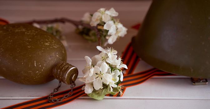 Composition to victory day. Soldier's flask, helmet and branches of apple trees and on a white background. banner size. High quality photo