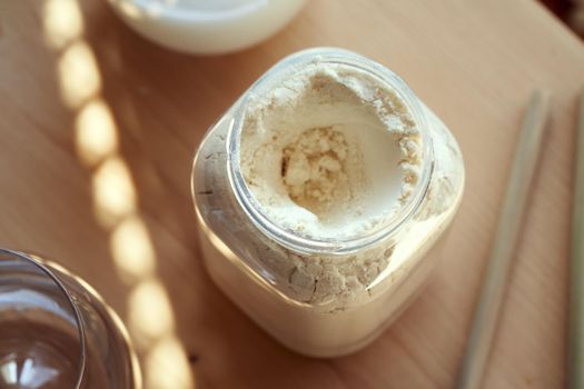 A jar of whey protein powder on a table, with a drink and bamboo straws in the background