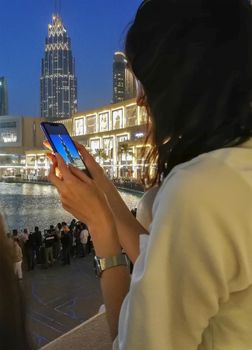 A girl takes photos on her mobile phone of the evening landscape with the sights of the city