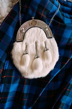 White fur sporran. A SPORRAN waist bag, decorative piece of Scots national clothing, made of white fur with three tassels. Lies on a blue checked kilt.