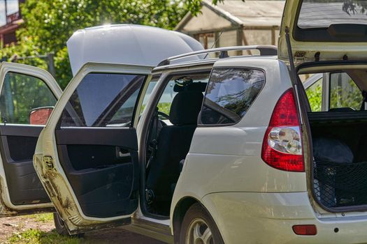 White car with open doors, trunk and hood stands on a garden plot. Airing the car