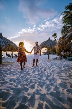 Palm Beach Aruba, Amazing tropical beach with palm trees entering the ocean against azur ocean, gold sand, and blue sky. man and woman walking at a white beach, mid age couple