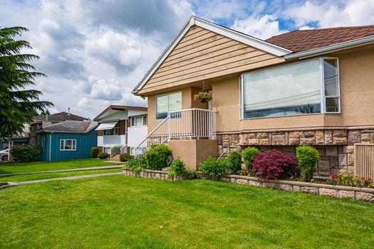 Modest family house with green lawn in front. Old residential house on cloudy day in Canada