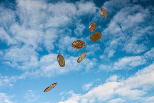 Coins falling from the sky against a background of white clouds