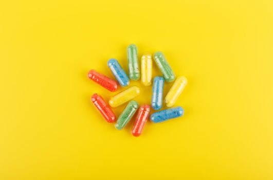 Flat lay with multicolored oval pills against yellow background. Concept of vitamins and wellbeing. Spilled pills flat lay on yellow background