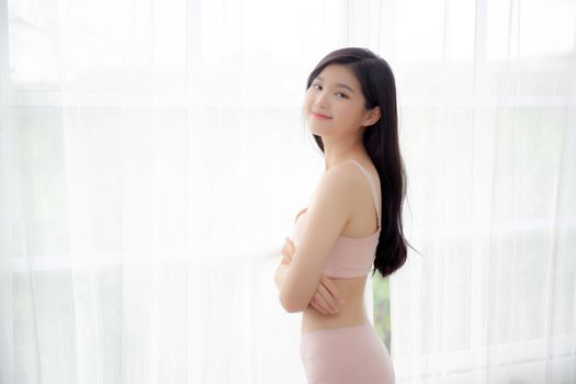 Beautiful portrait young asian woman sexy standing the window and smile while wake up with health, body of girl happy with freshness and cheerful with wellbeing, lifestyle and relax concept.