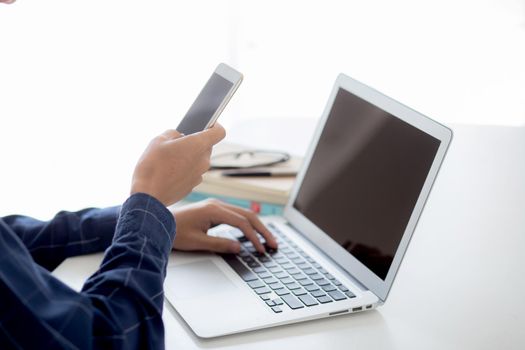 Hand of young man working with laptop computer and smartphone mockup on desk at home, notebook and phone display blank screen, freelance look message to internet, business and communication concept.