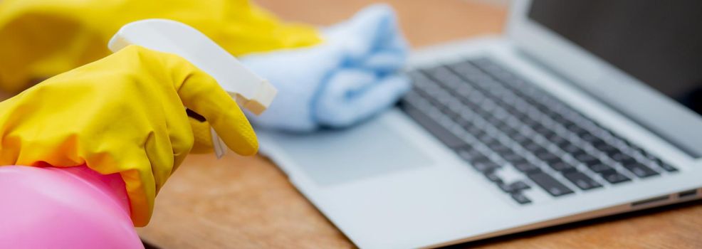 Hand of young asian woman cleaning and wipe laptop computer with disinfect and alcohol for protect pandemic covid-19 at home, girl in gloves cleaner notebook for hygiene, banner website.