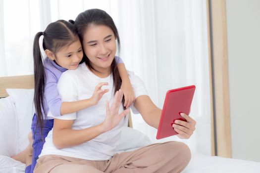 Young asian mom and daughter video call on tablet computer greeting with family together, happy mother and girl with relationship using technology in communication to internet online, two people.