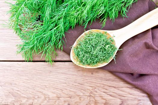 Dry dill in a spoon on a napkin, fresh herb on wooden board background from above